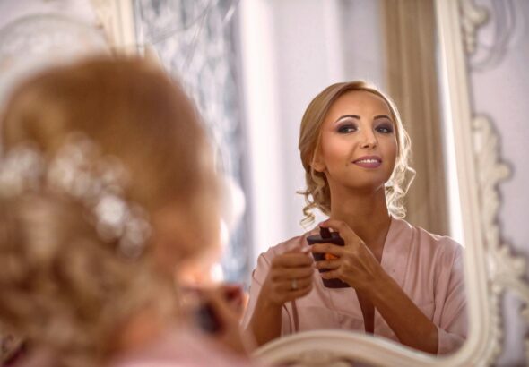 A sophisticated woman in a mirror reflection applying makeup, showcasing elegance and beauty.
